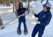 Two Denver Water employees with snowshoes strapped to their feet hold two metallic poles. 