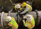 Four Denver Water workers place large conduit in place during a pipe replacement.  