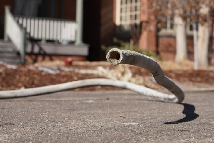 A lead pipe lays in the street in front of homes, the end of it raised toward the camera as if a snake seeking prey.