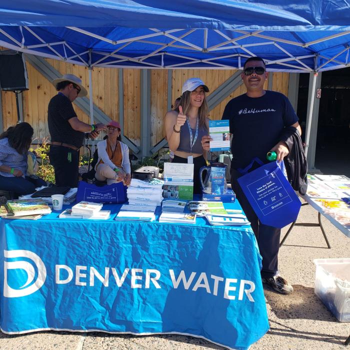 A group of people under a blue tent, with Denver Water on the table. A man is holding a box that has a filter in it. 