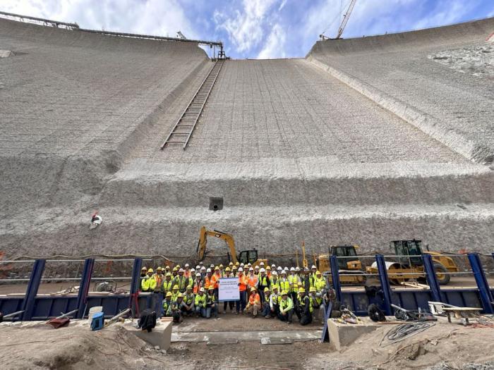 Dozens of people stand in front of a giant concrete dam