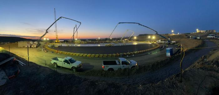 A night shot of construction workers pouring concrete, with the sunrise barely starting to be seen on the horizon.