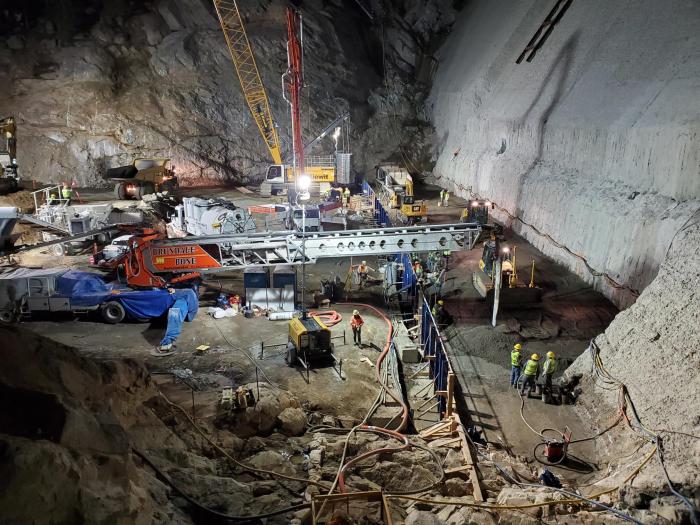 The construction site at the base of Gross Dam at night, busy with people and giant lights shining on the scene.