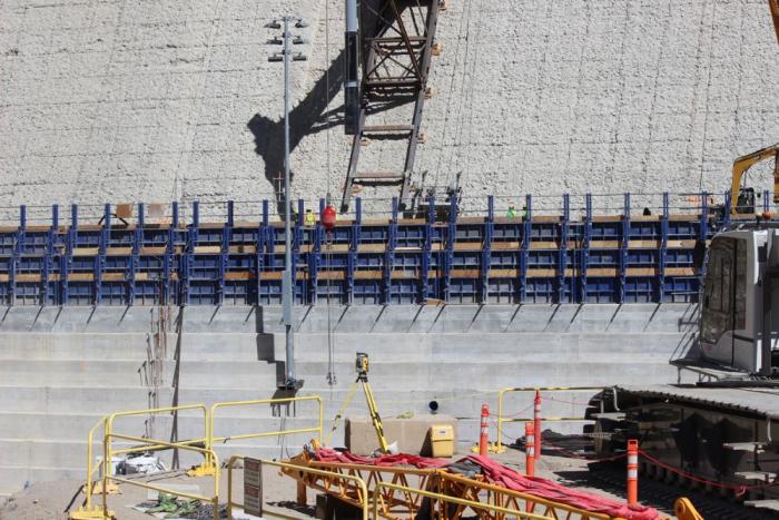 Heavy equipment work on the side of a concrete dam