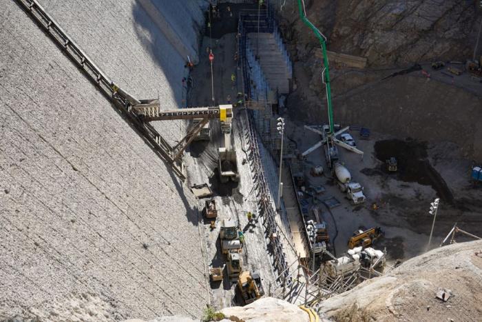 A view of heavy equipment from the top of a concrete dam 