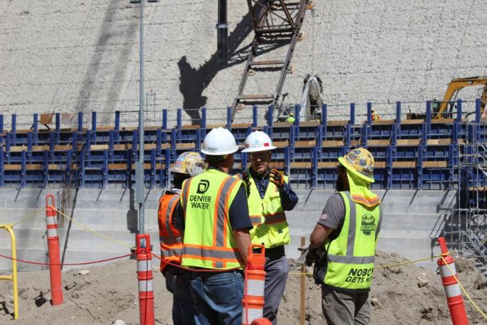 Four people in safety vests talk at the base of a dam