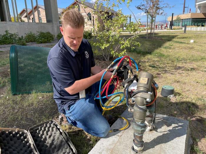 A man in a Denver Water polo shirt checks a device in the ground.