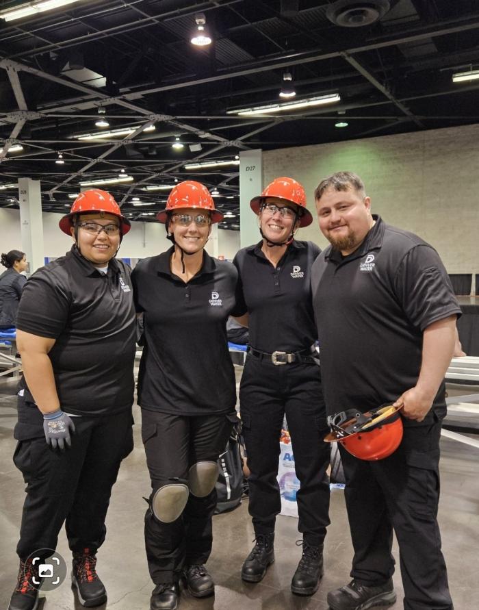 Three women in hard hats and a dark uniform, with a man in a similar uniform, smile for the camera.