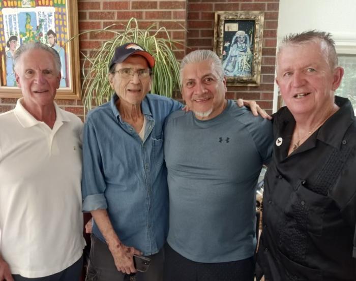 Four older men with their arms around each other, smiling for the camera.