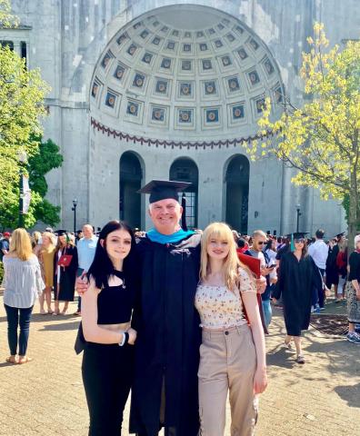 Man in cap and gown stands near daugthers