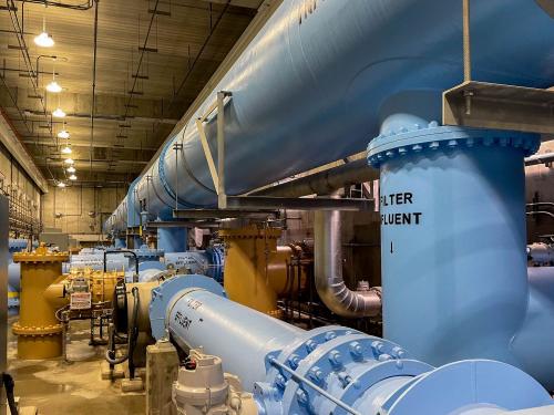 Large blue water pipes disappear into the distance in an underground, concrete-enclosed treatment plant.