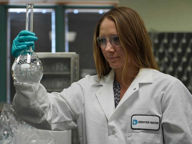 woman in lab coat looking at beaker of water