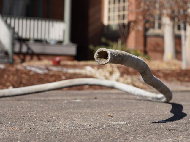 A lead pipe lays on the ground in front of homes, one end raised toward the camera as if it was a snake seeking prey.