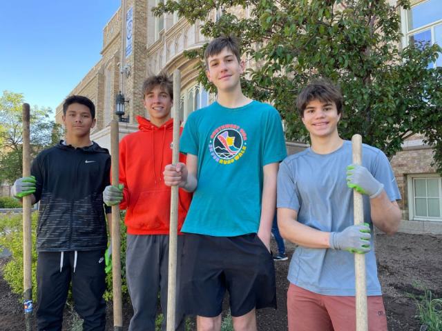 Four teenage boys holding shovels and hoes, smiling for the camera 